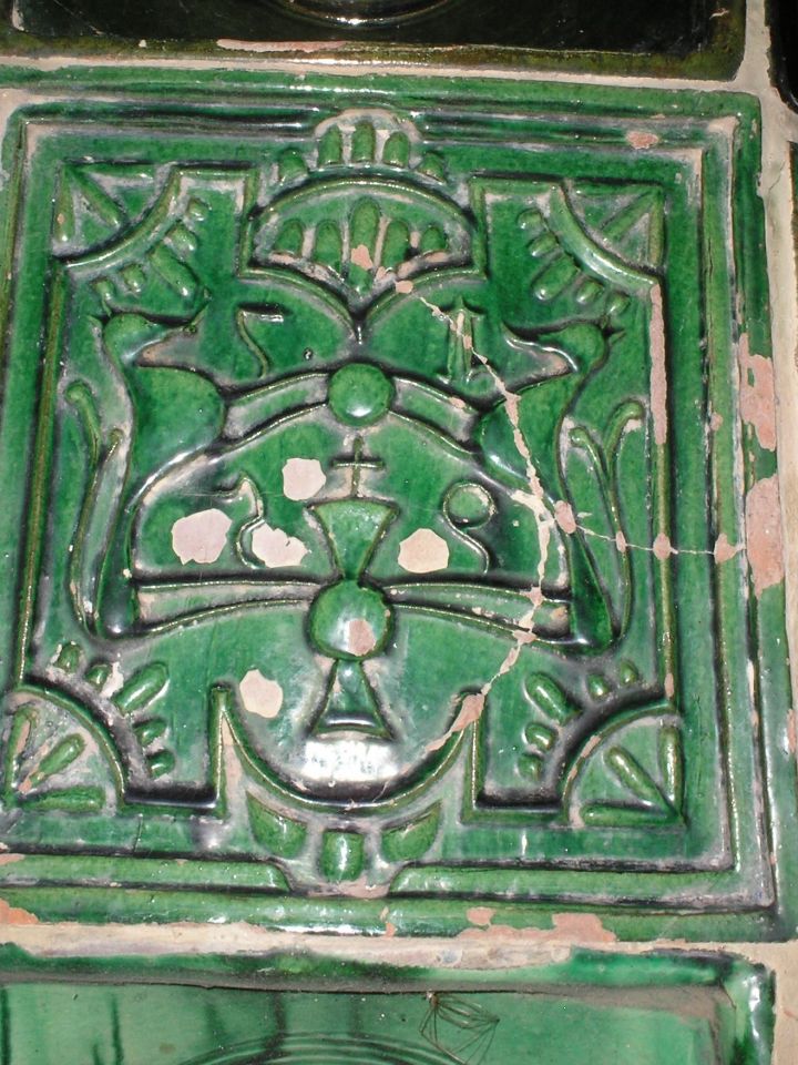 Segítünk: két állat (oroszlánok), keresztet/ kereket/illetve minden bizonnyal stilizált napszimbólumot fognak közre. A körülöttük látható 1795-ös évszám nem feltétlenül a kályhacsempe, sokkal inkább az adott nyomódúc készítési idejéről tanúskodik.