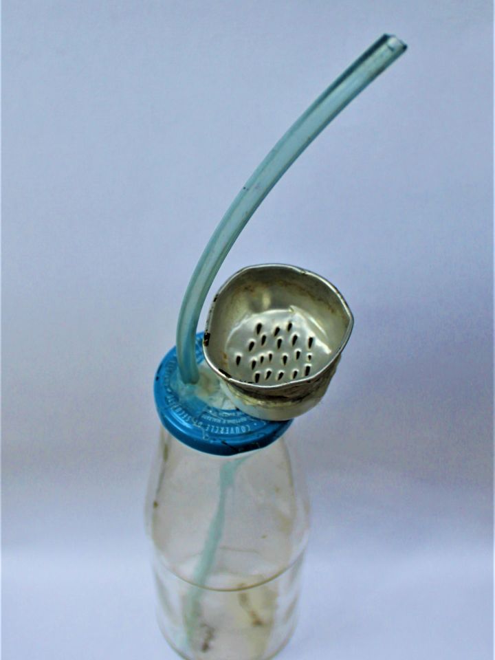 Házi készítésű szerkezet, boltban kapható keleti vízipipák mintájára. Átfúrt fémkupakos paradicsompürés üvegből, átlátszó benzincsőből, és a tetejére ragasztott fémszűrőből áll. Ltsz: 2010.1.3.