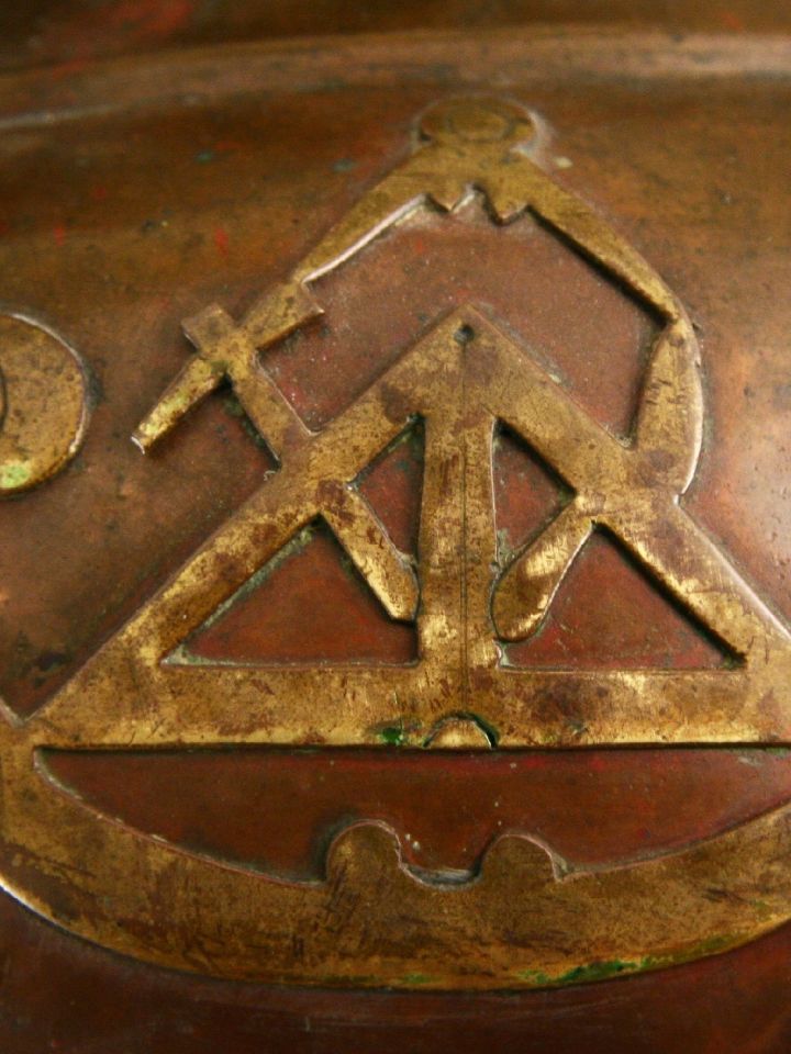 Rajta a kőművesekre utaló eszközökkel: derékszögmérő, kőműves kalapács, vakolókanál, körző.