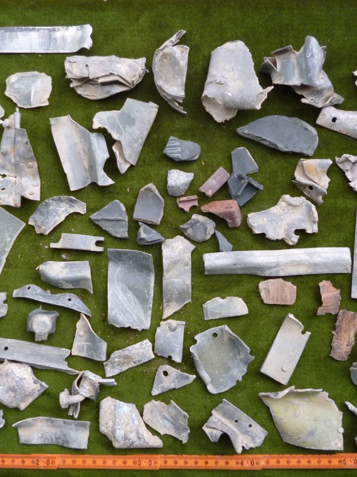 Összesítő kép a begyűjtött leletanyagról. Bal oldalon a pilótakabin ablakából származó plexidarabok, jobb oldalon  vas hevedertagok töredékei a csatarepülőgép V-Ya Volkov Yartsev 23 mm űrméretű gépágyúiból és a 12,7 mm űrméretű UBT géppuskából